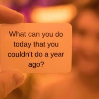 Hand holding a card that says, "What can you do today that you couldn't do a year ago?"
